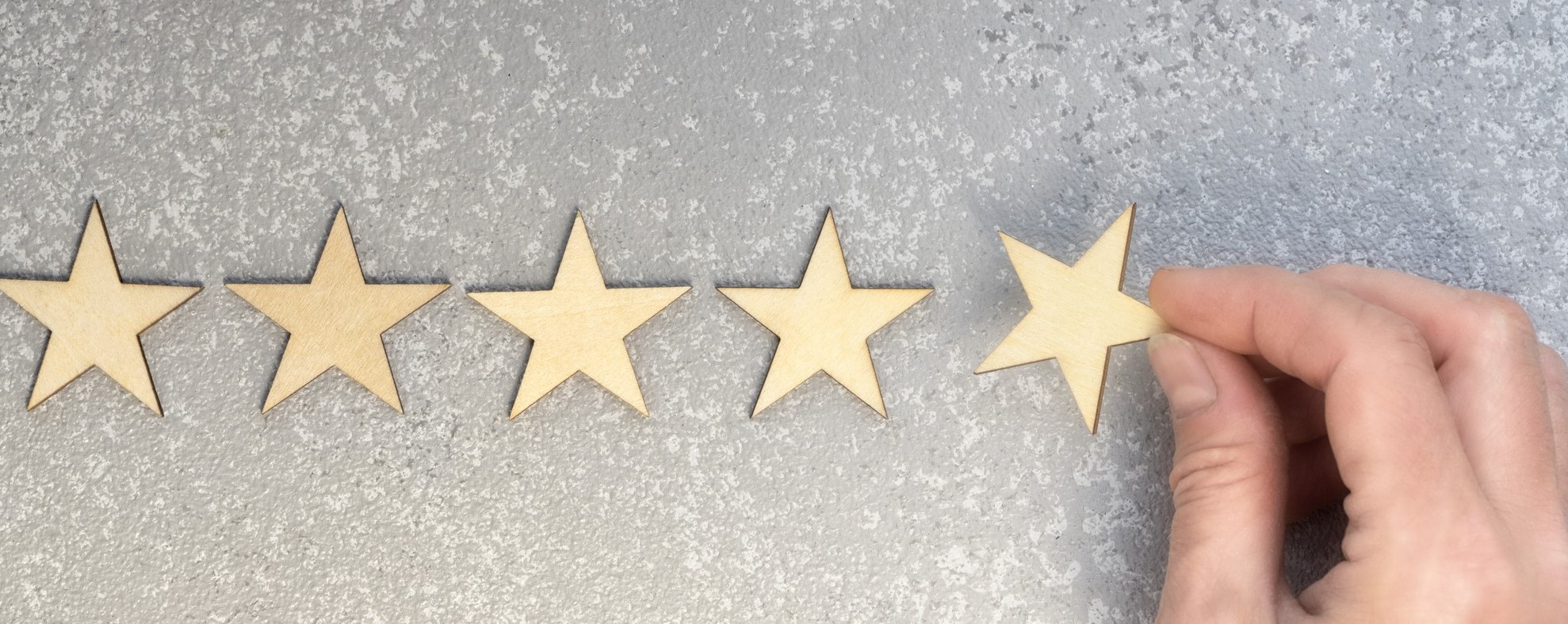 five wooden stars and hand putting the last one to increase rating on a silver background, top view with copy space
