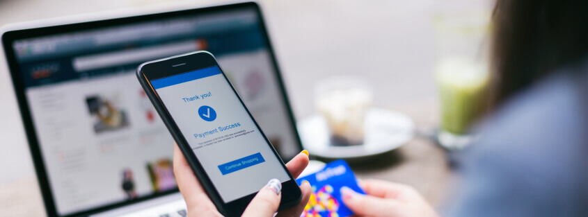 Women's hand holding a mobile phone and checking out of an eCommerce store.