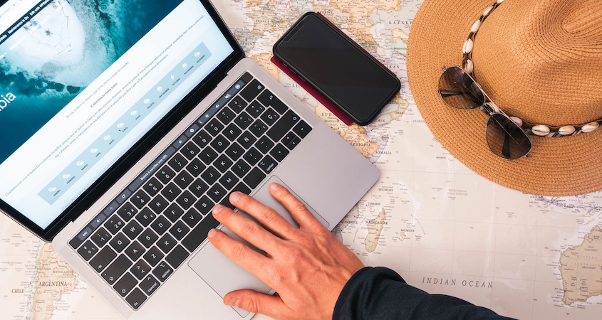 booking travel on laptop on top of a world map with phone hat sunglasses