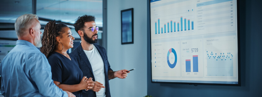 Man presenting to two colleagues with a presentation on a large TV monitor