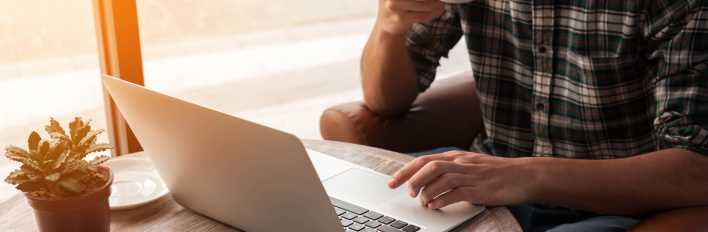 plaid shirt person on laptop with coffee 708x232 1 4