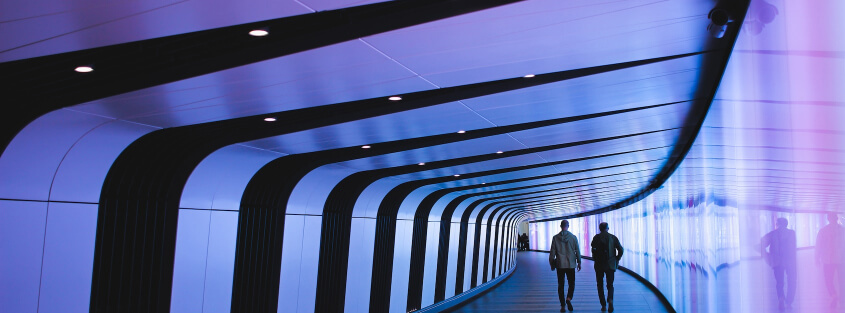 Two people walking down a long hallway with colorful paneling